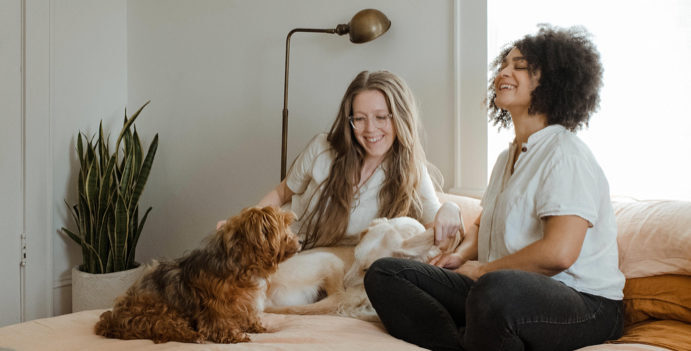 A Couple of Women Sitting on Top of a Bed With Two Dogs