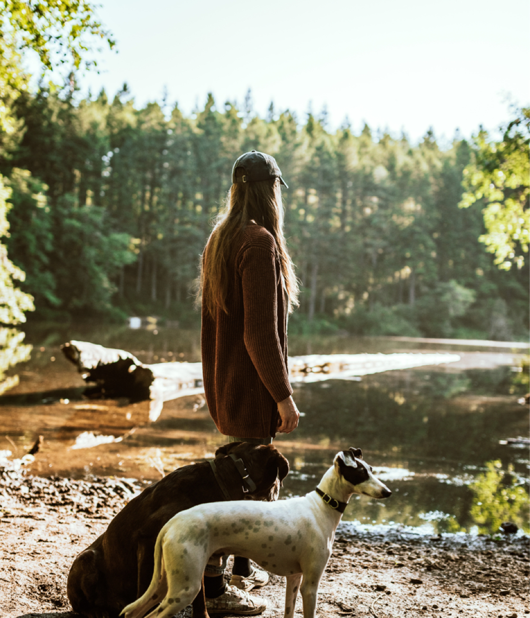 A Woman Standing Next to Two Dogs Near a River