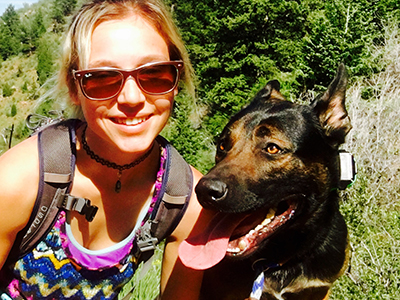 Woman Wearing Colorful Tank Top, Backpack And Sunglasses Smiling With Dog Looking Away
