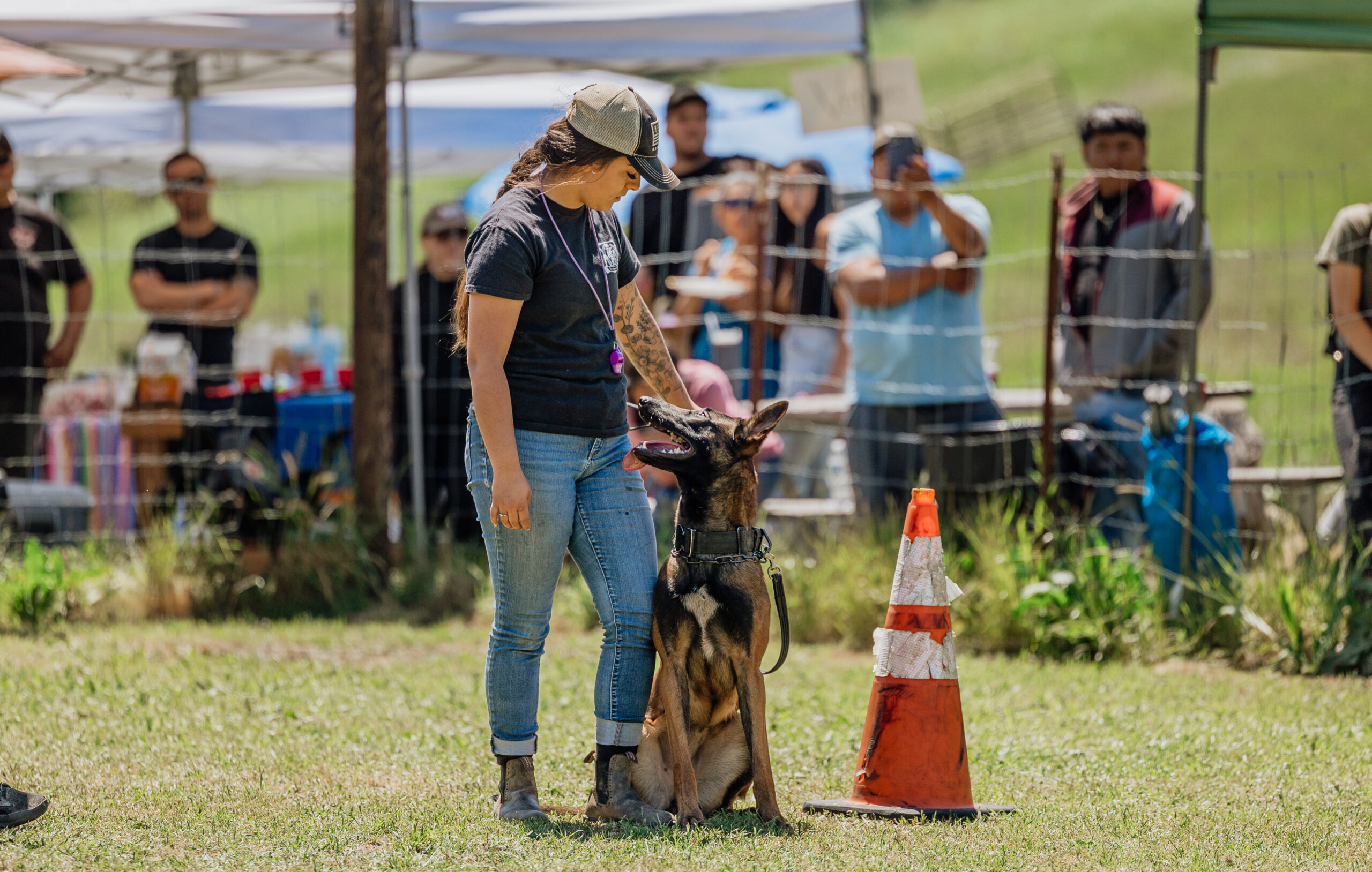 Woman With Beige Cap Looking At Her German Shepherd Sitting Next To A Pylon