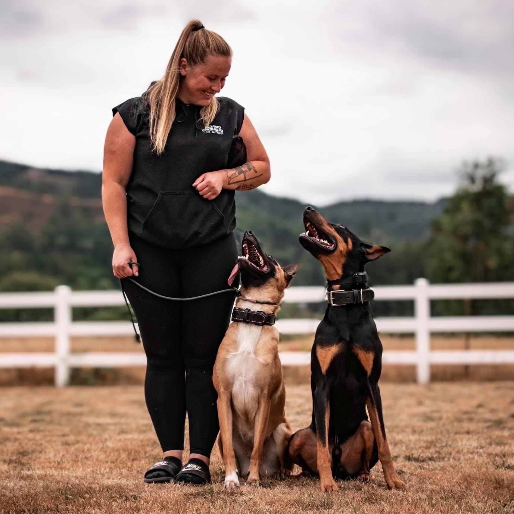 Woman Standing Next To Two Black Dogs On Leashes In Front of A Magnolia Tree In The Fog